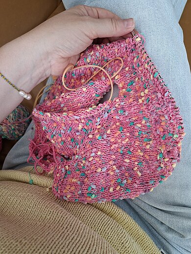 Ein farbenfrohes Strickprojekt in Rosa mit bunten Akzenten auf der Rundstricknadel.