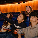 Kinder und Jugendliche sitzen im Planetarium und schauen in den Sternenhimmel in der Planetariumskuppel.
