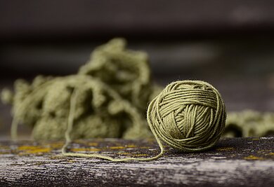 Woolness Aufbaukurs – Mustermix und Farbspektakel Grüner Wollknäul mit angefangenem Strickstück.