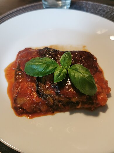 La Cucina Siciliana - authentisch & aromatisch kochen mit Antonio   Auf einem weißen Teller wird eine sizilianische Hauptspeise aus Aubergine serviert.