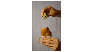 Pescadillas Zwei Hände sind zu sehen. In der einen Hand wird ein Pescadilla gehalten. Die andere Hand träufelt auf diese einen Saft von Limette.