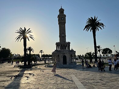 Türkischer belebter Platz mit Uhrturm in der Mitte und Palmen. 
