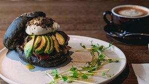 Burger mit Avocados, daneben eine Tasse Cappuccino