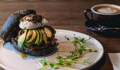 Burger mit Avocados, daneben eine Tasse Cappuccino