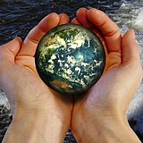 Zwei Hände mit Handfläche nach oben halten eine kleine Weltkugel  