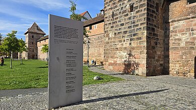 Eine Gruppe von Menschen geht auf einem gepflasterten Weg. Einige Personen halten Hände, während andere alleine oder in Gruppen gehen. Lange Schatten fallen auf den Boden.