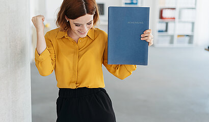 Frau hat eine Bewerbungsmappe in der Hand und freut sich.