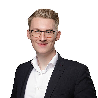 Ein Portraitbild der Kursleitung Kai Wegwerth. Er blickt mit blauen Augen lächelnd in die Kamera. Sein Haar ist blond, seine Brille ist eckig und er trägt ein Jacket.