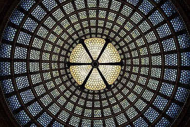 Kuppeldecke mit symmetrischem Muster aus kleinen Glasfenstern und zentraler runder Lichtquelle
