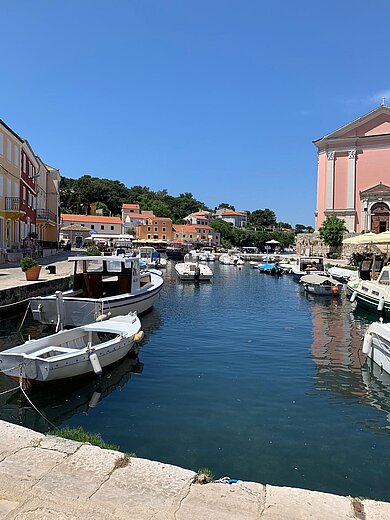 Eine sonnige Hafenbucht mit kleinen Fischerbooten umgeben von bunten Häusern.