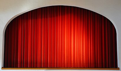 Ein geschlossener roter Theatervorhang auf einer kleinen Bühne