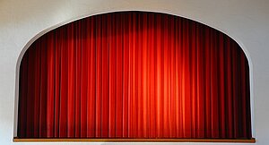Ein geschlossener roter Theatervorhang auf einer kleinen Bühne