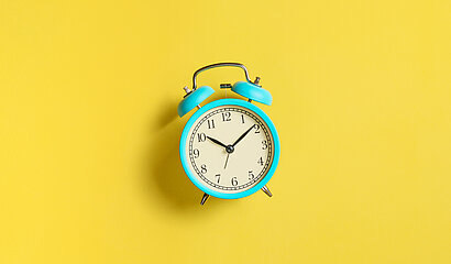 Mintgrüner Wecker vor gelbem Hintergrund