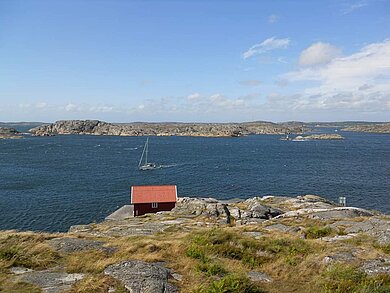 Kleines Holzhaus in den schwedischen Schären auf einem Hügel, dahinter die blaue Ostsee.