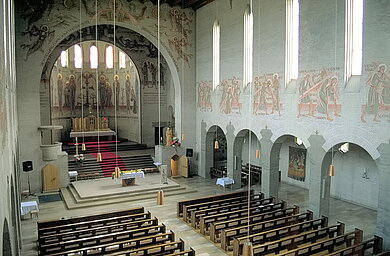 Kirchenraum von innen mit Altar im Hintergrund und vorne im Bild die hölzernen Sitzreihen