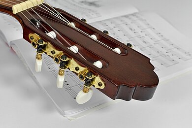 Klassische Gitarre mit Noten  Kopf einer Gitarre mit Wirbeln und Saiten auf Notenblättern.