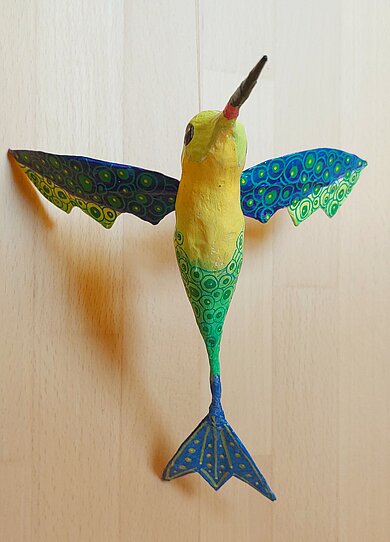 Bunter Vogel mit gelben Kopf aus Pappmaschee mit ausgebreiteten blau-grünen Flügeln