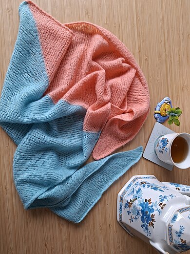 Ein zweifarbiges, gestricktes Tuch in Rosa und Türkis, arrangiert mit Teetasse und Teekanne.