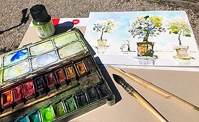 Aquarellieren in den Hesperidengärten Blick auf ein aquarelliertes Bild mit 3 Kübelpflanzen, im Vordergrund ein Aquarellmalkasten und verschiedene Pinsel.