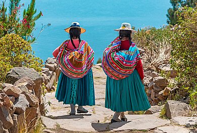 Zwei indigene Frauen in Tracht gehen einen Steinweg hinunter zum Hafen der Isla Taquile im Titicaca See, Peru.