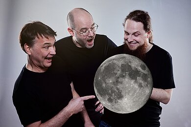 Foto der drei Akteure, die ein Modell des Mondes halten. 