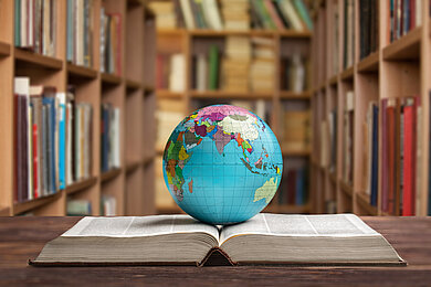 Globus auf einem aufgeschlagenen Buch vor einem Bücherregal