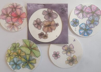 Das Bild zeigt fünf kleine runde Aquarellzeichnungen von bunten Blumen in zarten Rosa-, Blau-, Grün- und Lilatönen auf hellem Hintergrund.