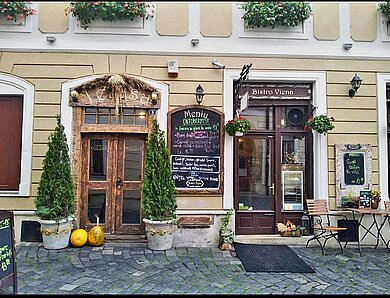 Eine Fassade mit zwei Eingängen zu Restaurants, einladend begrünt und mit aushängender Speisekarte auf Rumänisch.