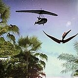 Eine Dschungellandschaft aus Zeiten der Dinosaurier. In der Luft befindet sich ein Flugsaurier, über dem ein Drachenflieger fliegt (animiert).
